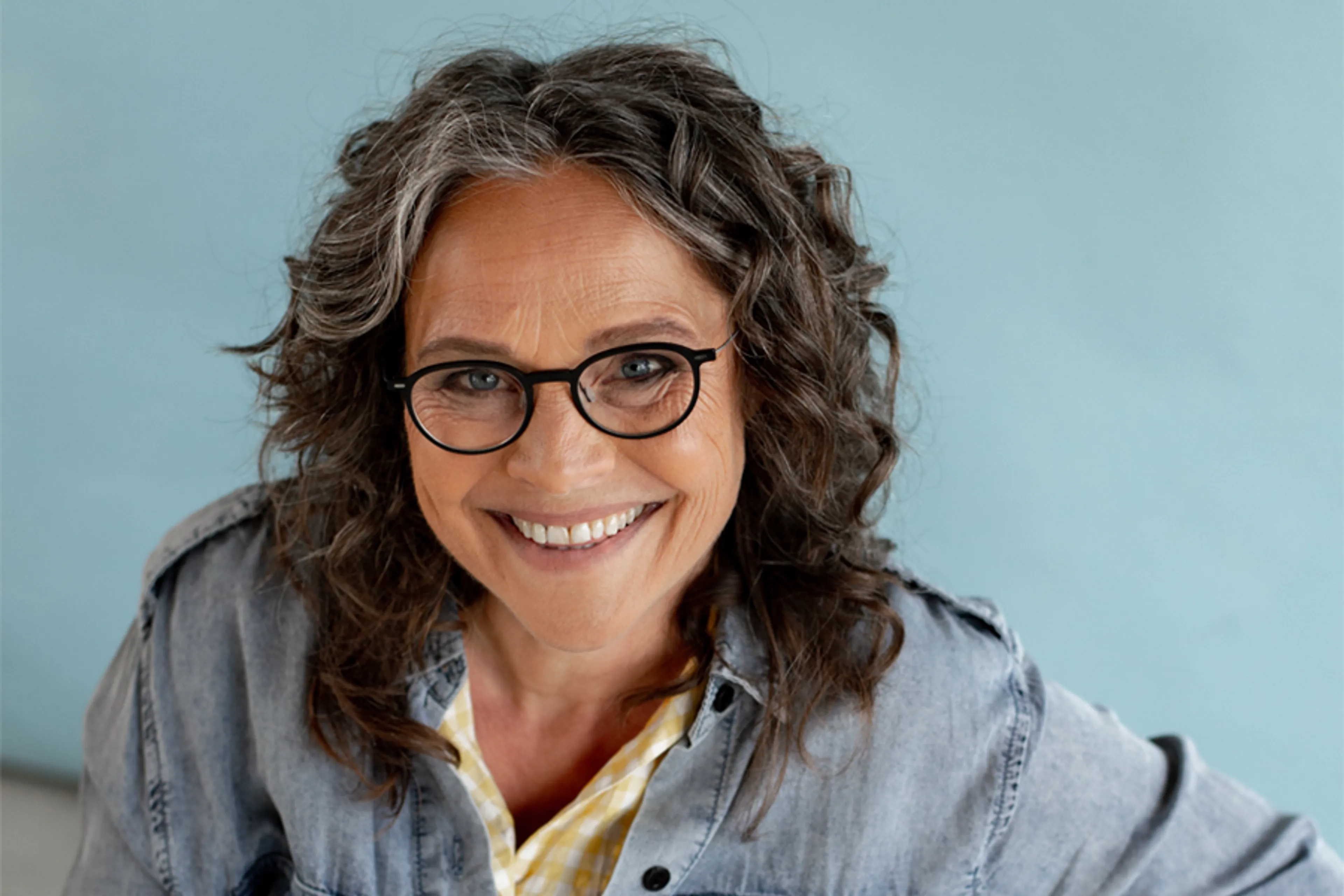 Op de foto staat Dianne, lachend naar de camera. Ze heeft donkere, grijze krullen tot schouderlengte. Ze heeft een spijkerblouse aan en heeft een bril op.